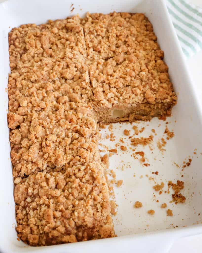 An 11x7 inch baking dish full of apple coffee cake with a couple of pieces removed. 
