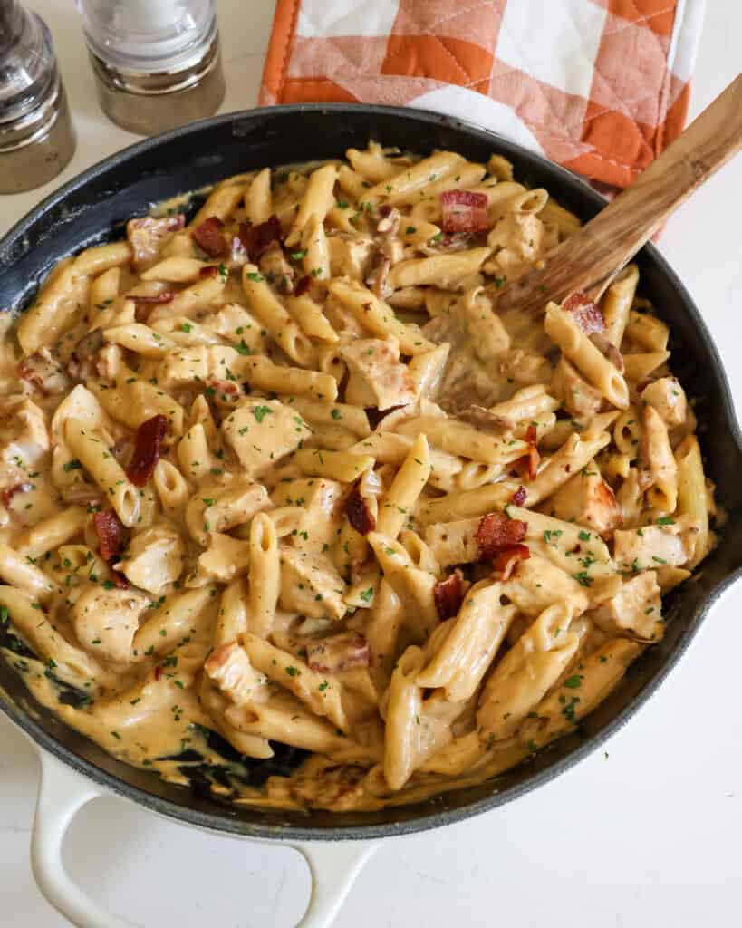 A large black skillet full of chicken bacon ranch pasta with a salt and pepper shaker in the background. 