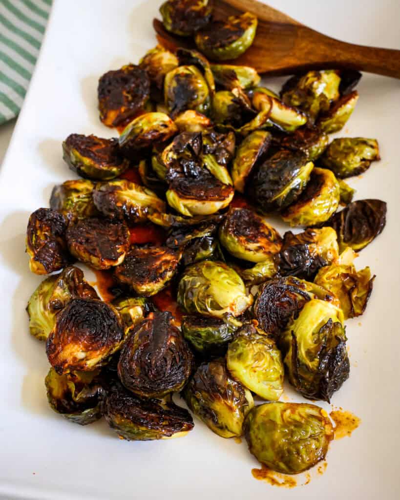 Crispy Brussels sprouts on a white serving platter with a wooden spoon.