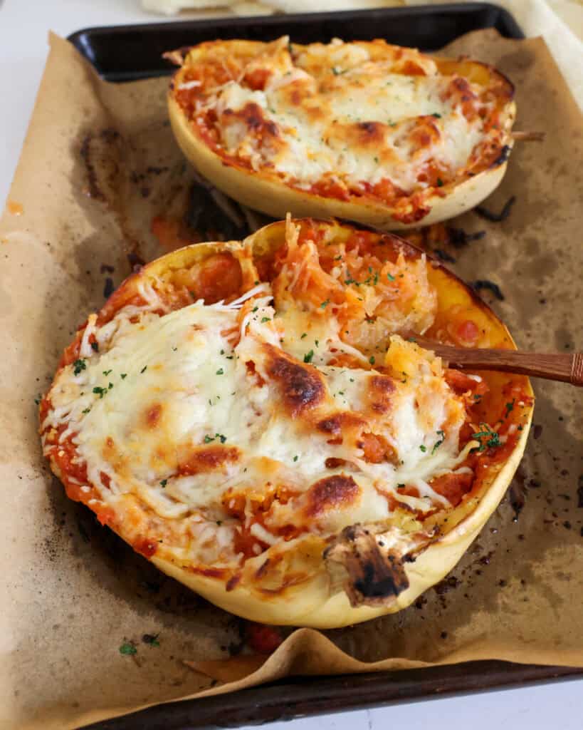 Two halves of roasted spaghetti squash mixed with marinara sauce and topped with mozzarella cheese. 