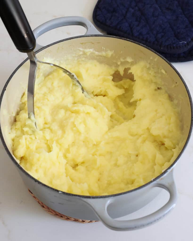 A Dutch oven full of mashed potatoes with a potato masher in the pot. 