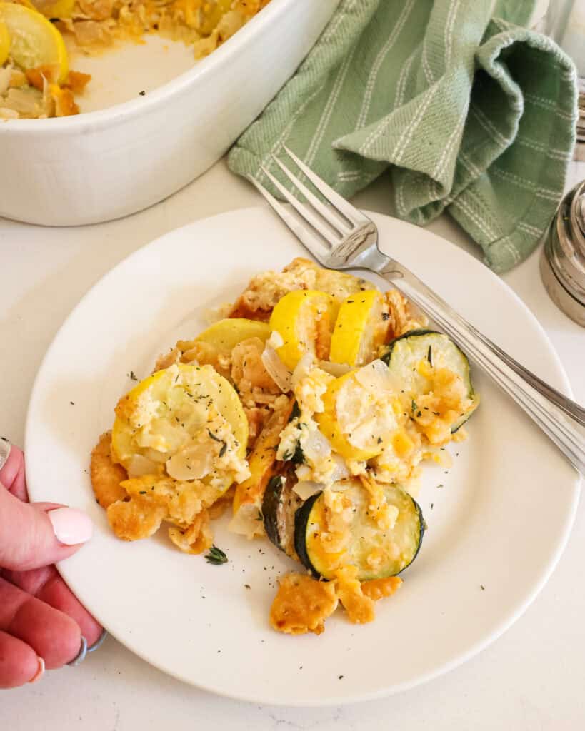 Squash casserole on a single serving plate with a fork and the rest of the casserole in the background