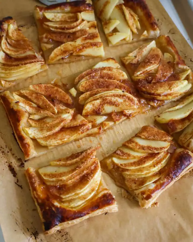 A cut apple tart on a parchment paper covered baking sheet.