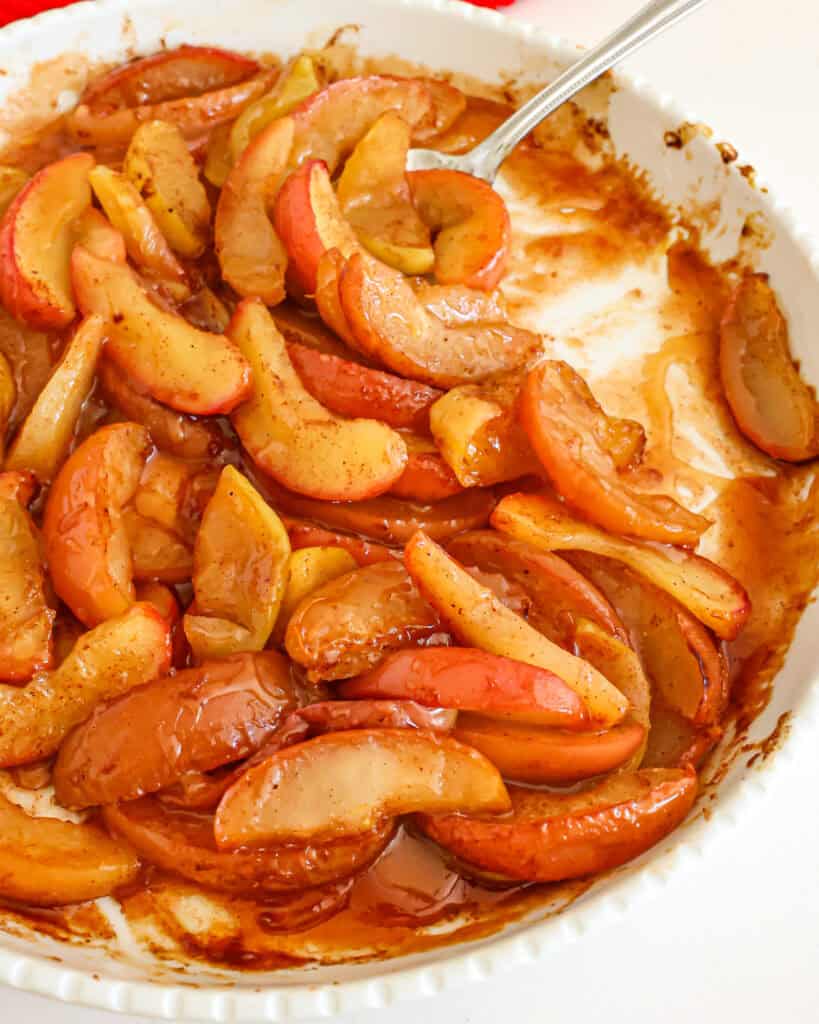 Baked apples in a round serving dish with a spoon in it. 