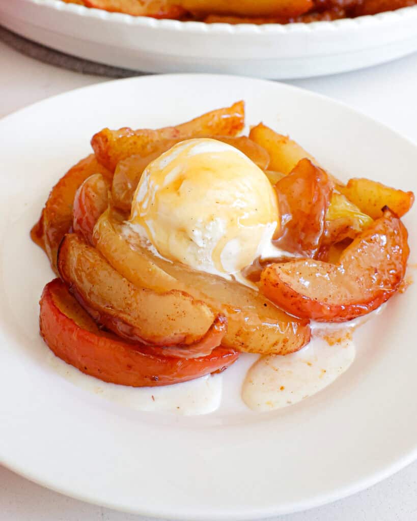 Baked apples on a single serving white plate with a scoop of vanilla ice cream and caramel sauce on top.