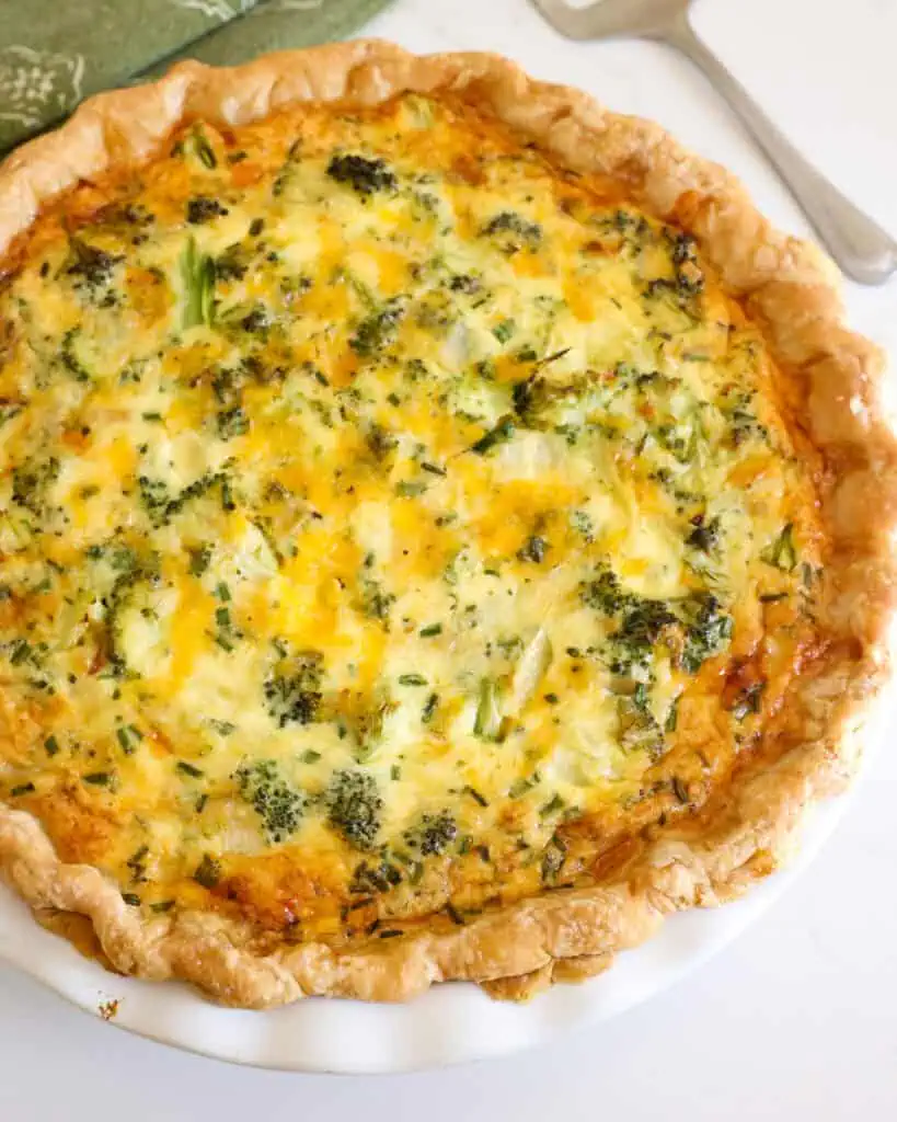An overhead views of a broccoli quiche with a pie server and green towel in the background.