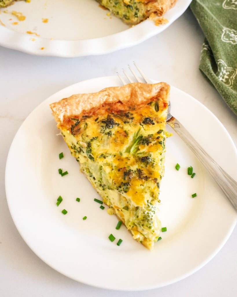 A slice of broccoli quiche on a plate with chopped chives and a fork. 