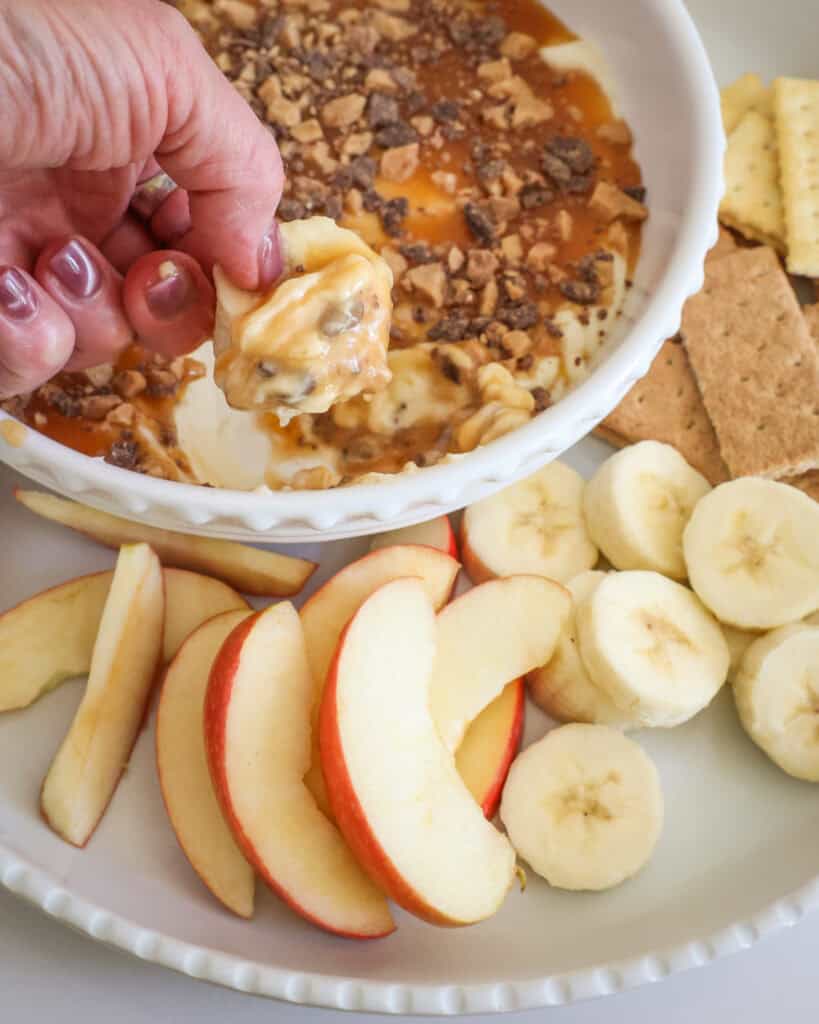 A banana slice dipped in a bowl full of caramel apple dip. 