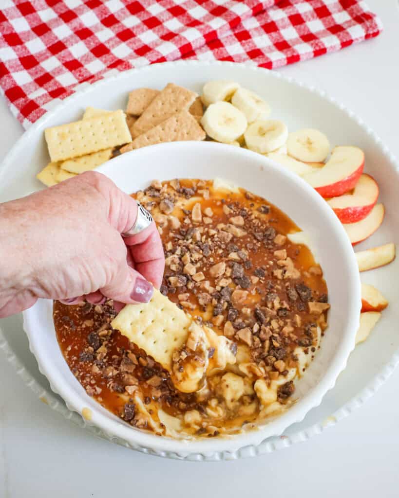 An overhead view of caramel apple dip with a savory cracker dipped in it. 