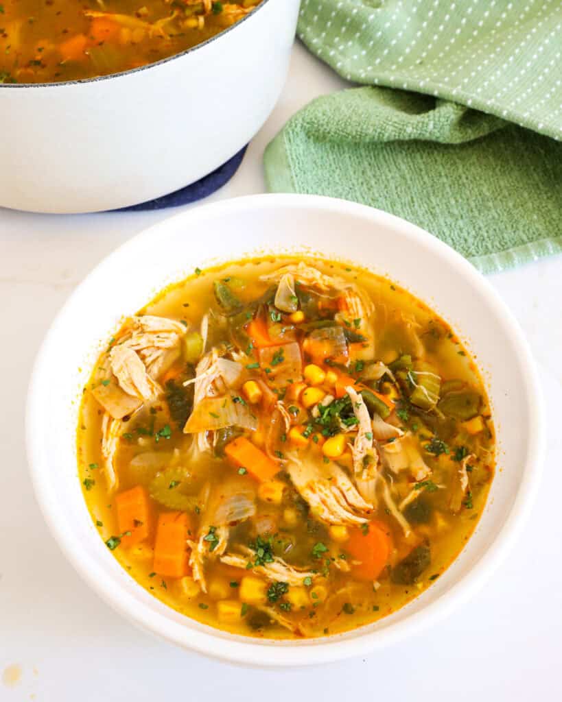 A white serving bowl full of chicken poblano soup with a green kitchen towel in the background. 