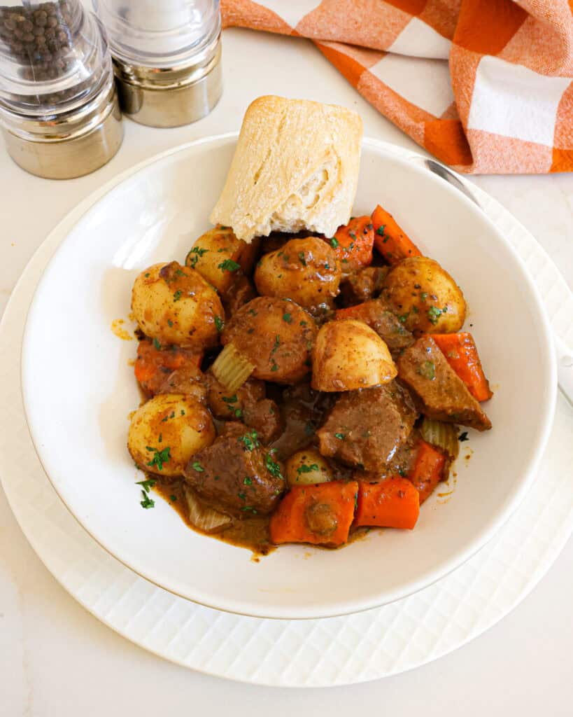 Beef stew in a single serving bowl with a piece of crusty French bread. 