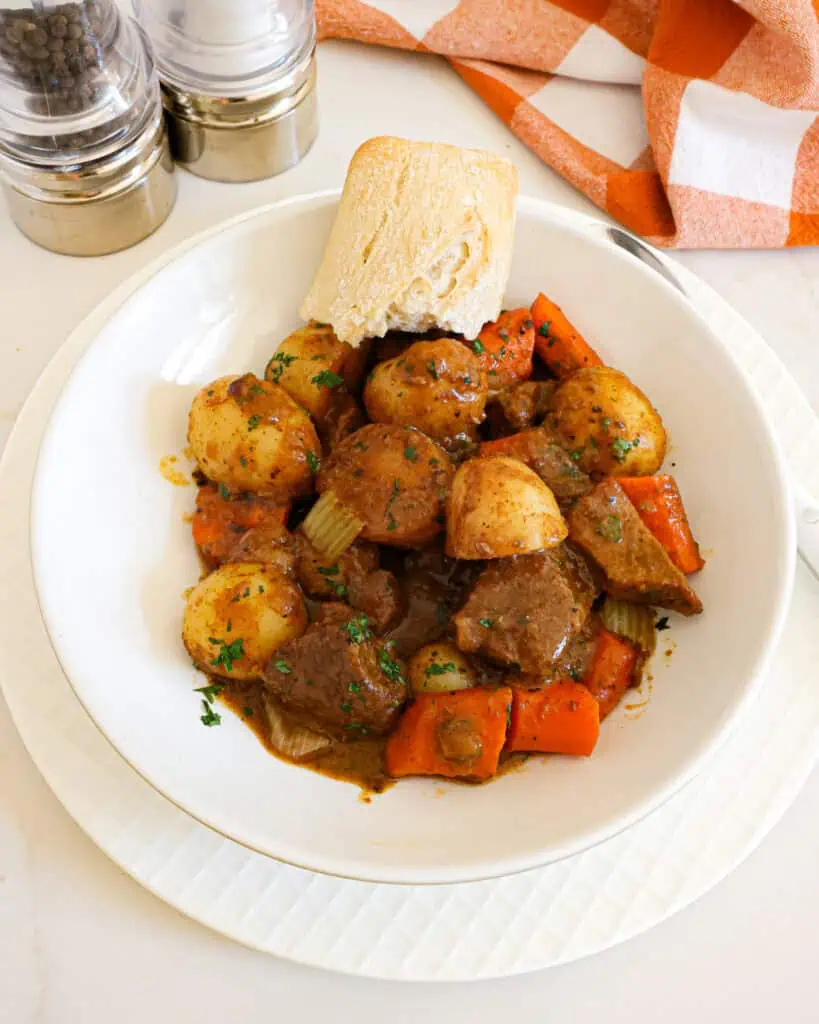 Beef stew in a single serving bowl with a piece of crusty French bread. 