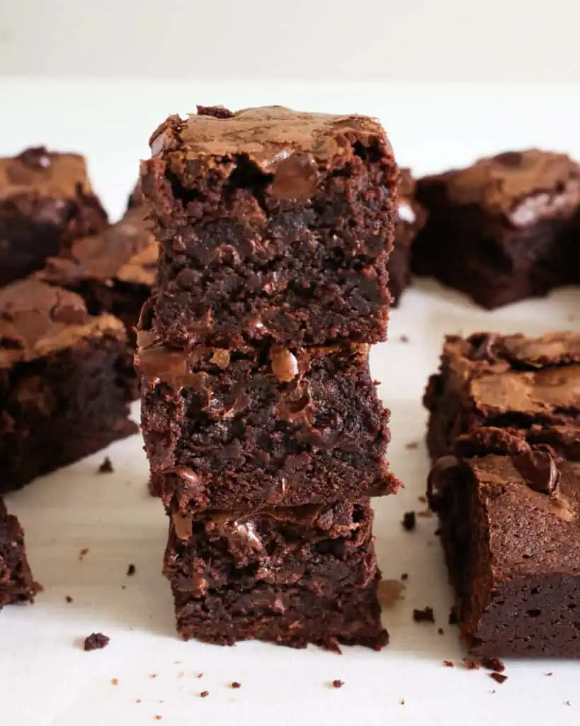 Stacked brownies on a cutting board covered with parchment paper.