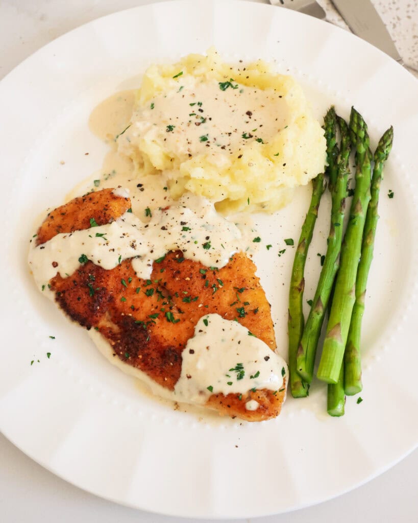 Garlic parmesan chicken on a single serving plate with mashed potatoes and asparagus. 