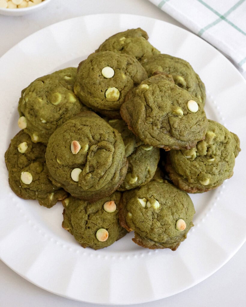 A plate full of matcha cookies with white chocolate chips with a bowl of chocolate chips in the background.