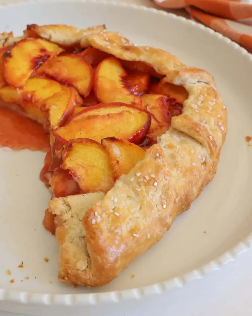 A peach galette with several pieces missing on a round white serving platter.