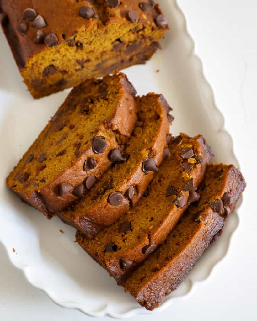Four slices of pumpkin chocolate chip bread stacked on a diagonal on a platter with the rest of the loaf of the bread. 