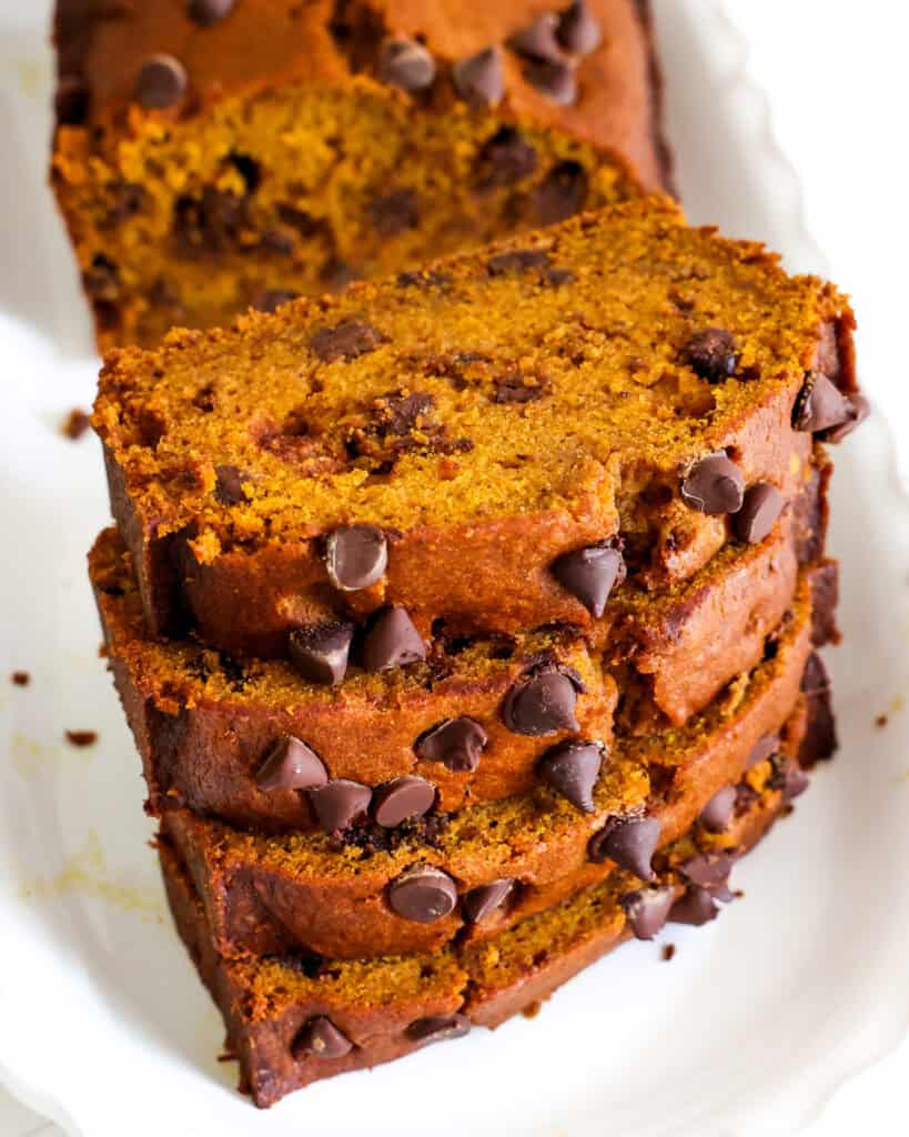 Four slices of pumpkin bread with chocolate chips with the rest of the loaf on a white erving platter. 