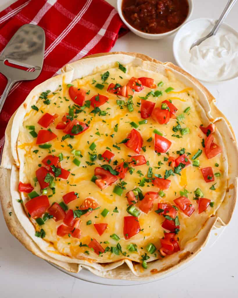 An overhead view of taco pie with a pie server, and sour cream and salsa bowl in the background.