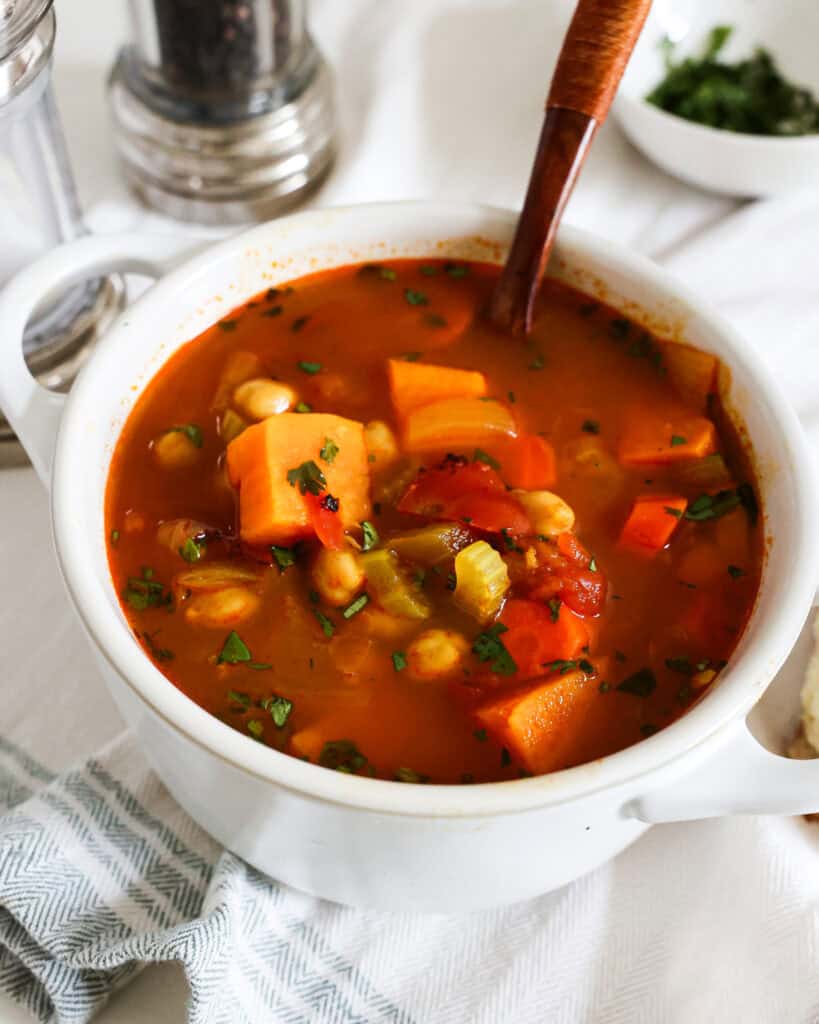 A single serving white soup bowl full of chicken pea soup with a salt and pepper shaker in the background. 
