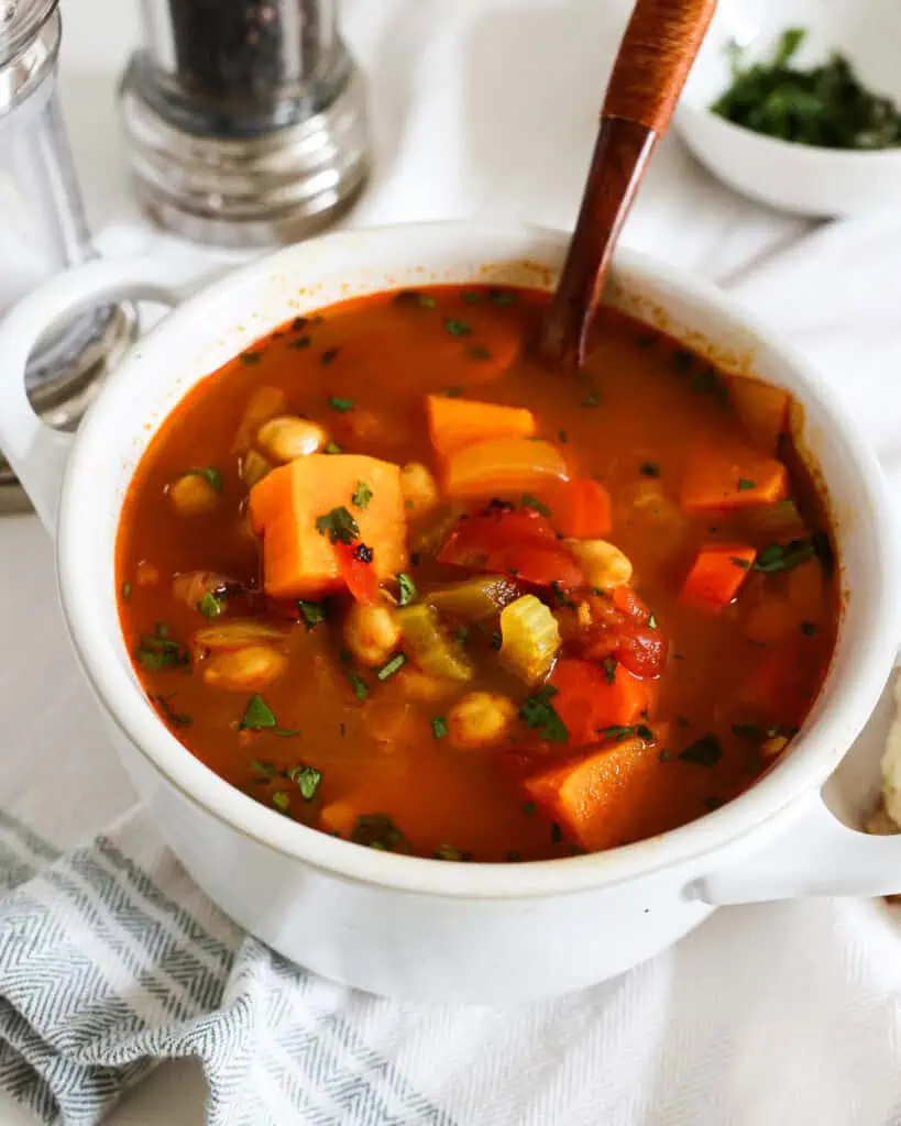 A single serving white soup bowl full of chicken pea soup with a salt and pepper shaker in the background. 