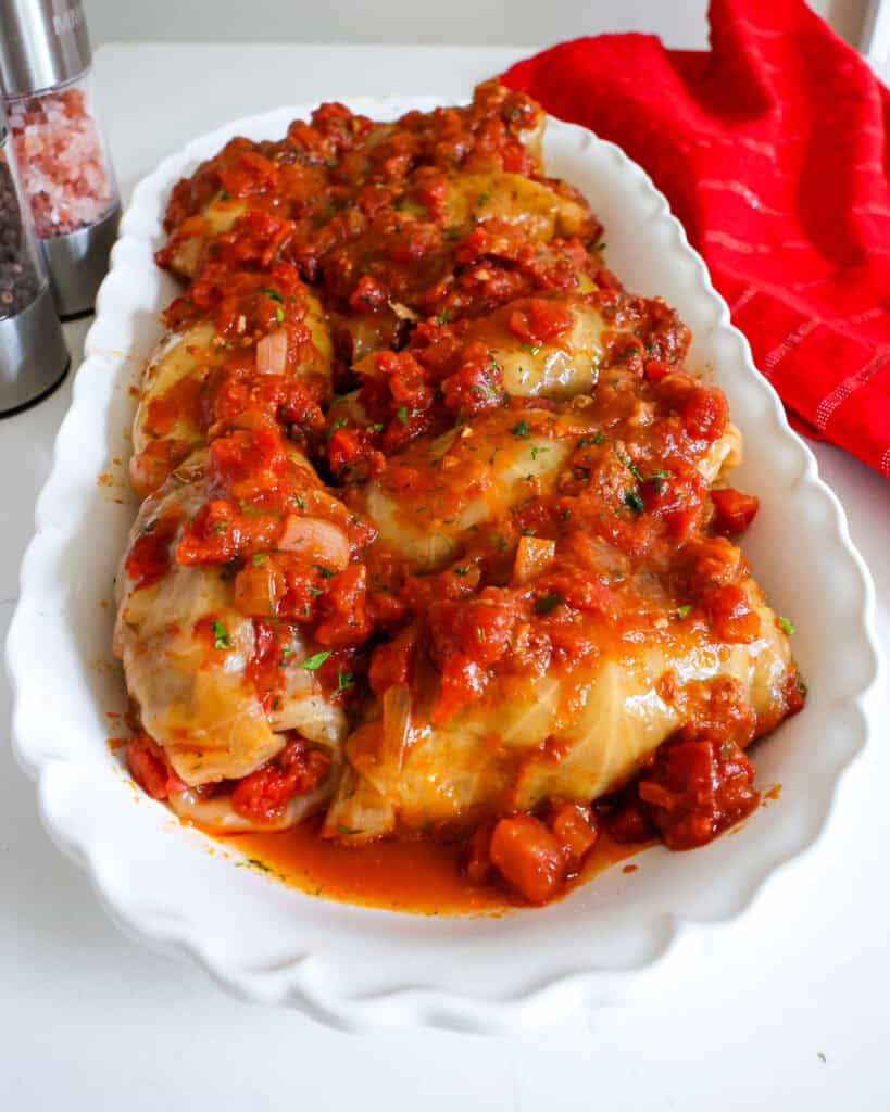 A close up view of crock pot cabbage rolls on a serving platter with tomato sauce. 
