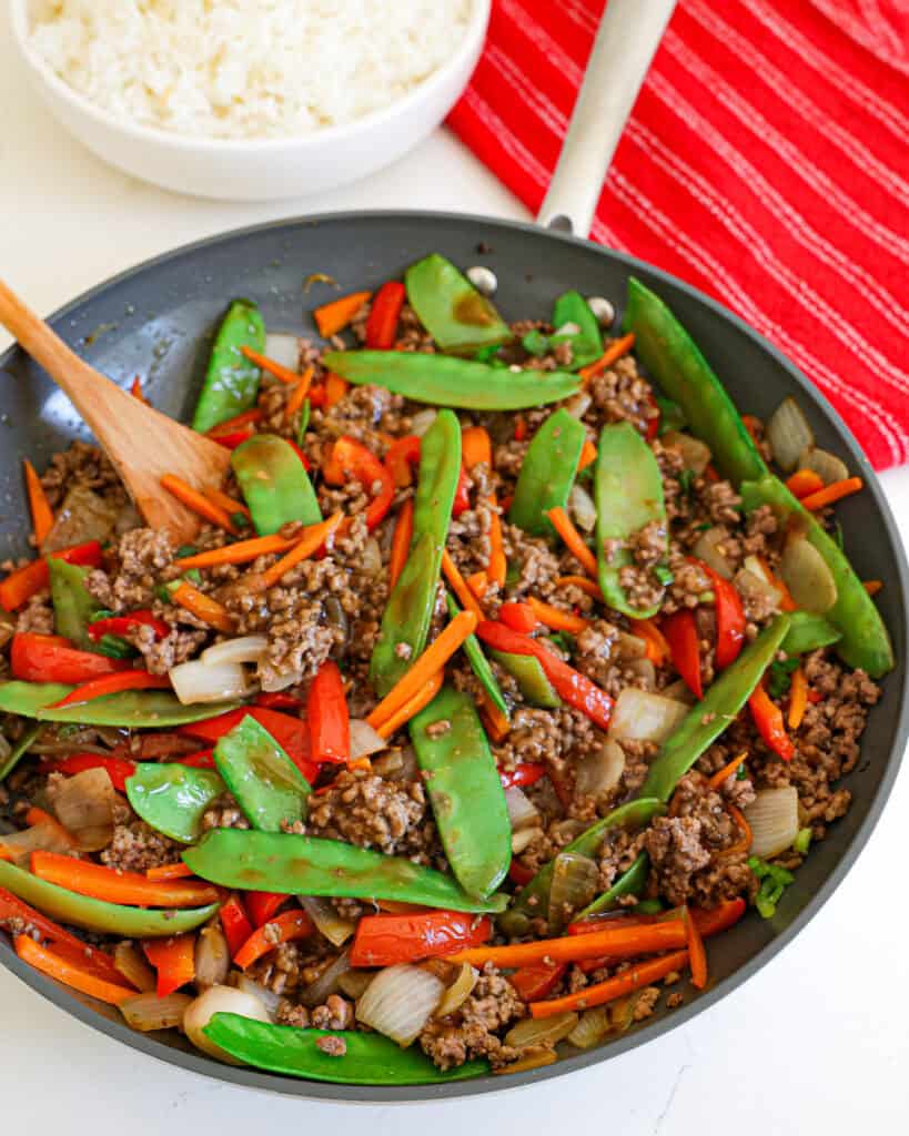 A close up view of ground beef stir fry with onions, carrots, red bell pepper, and snow peas. 