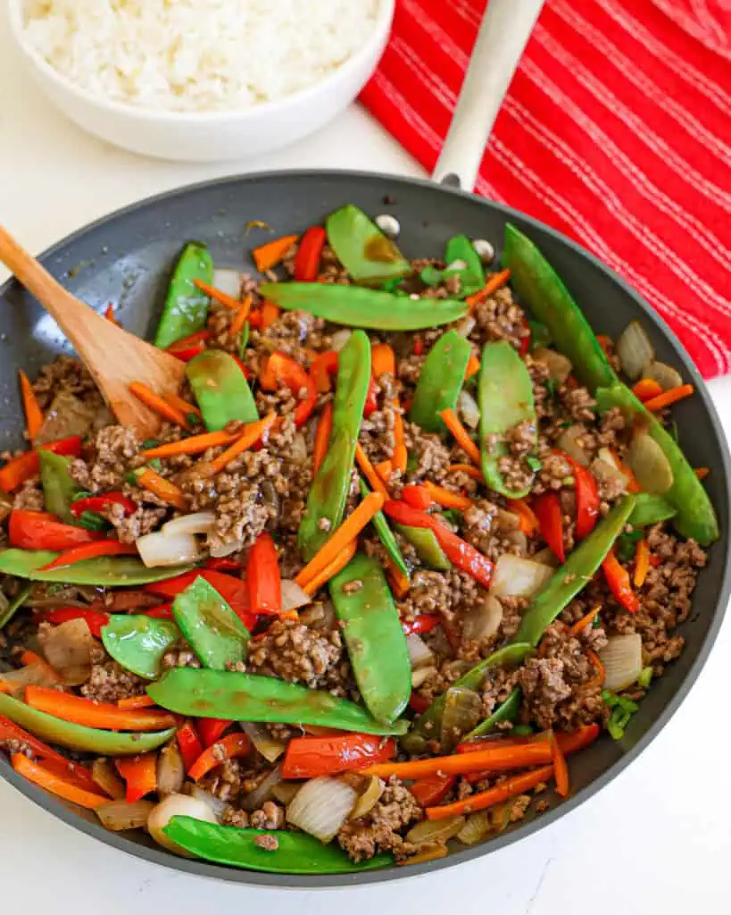 A close up view of ground beef stir fry with onions, carrots, red bell pepper, and snow peas.
