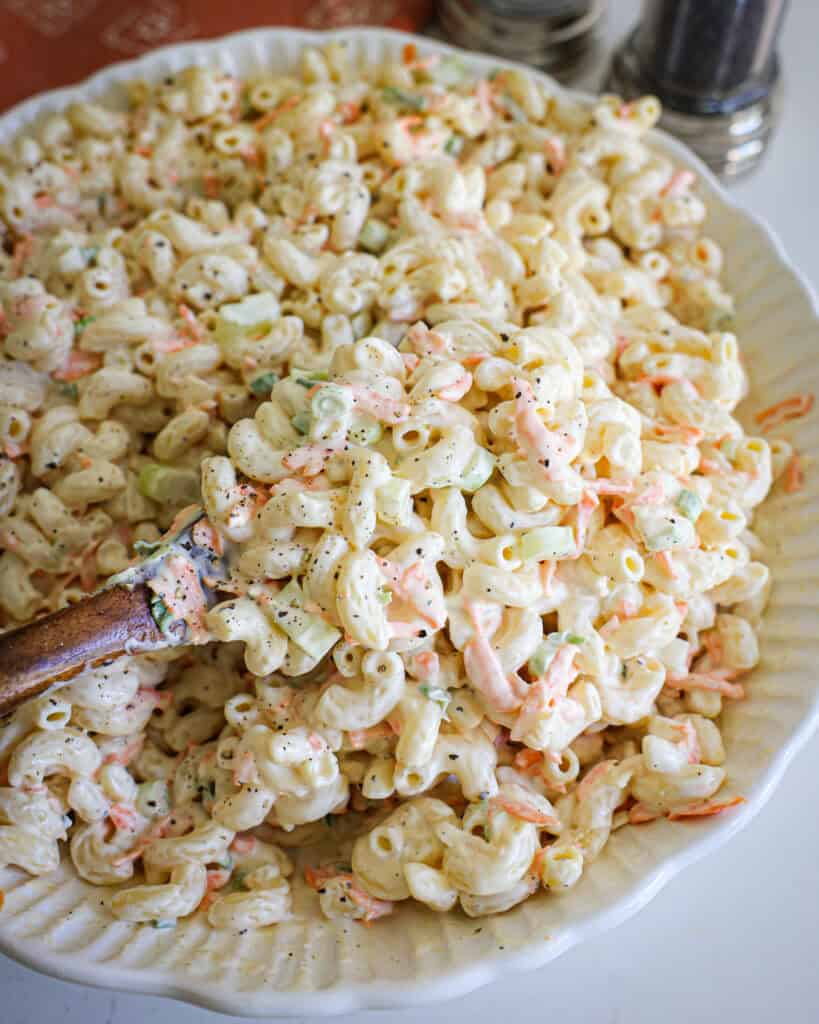 A serving bowl and a wooden spoon full of macaroni salad. 