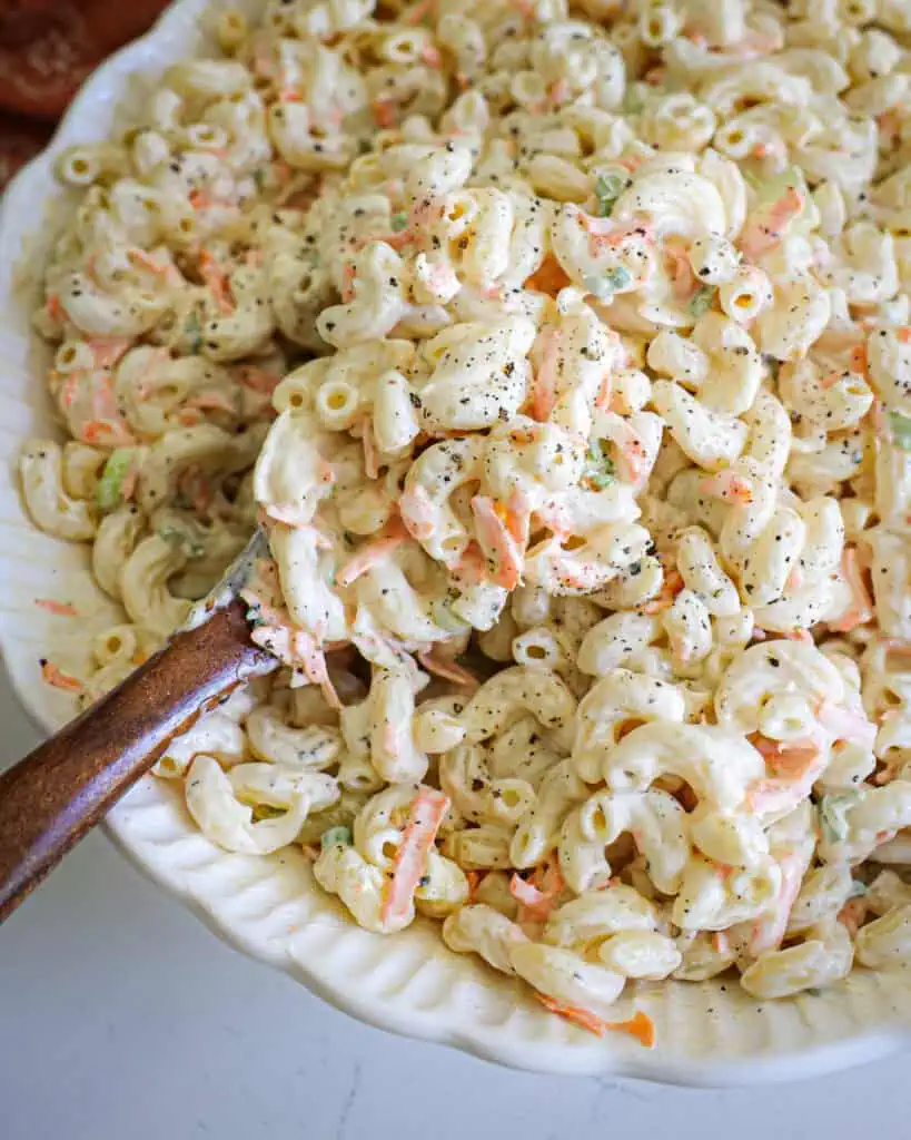 A white scalloped serving bowl full of Hawaiian macaroni salad.