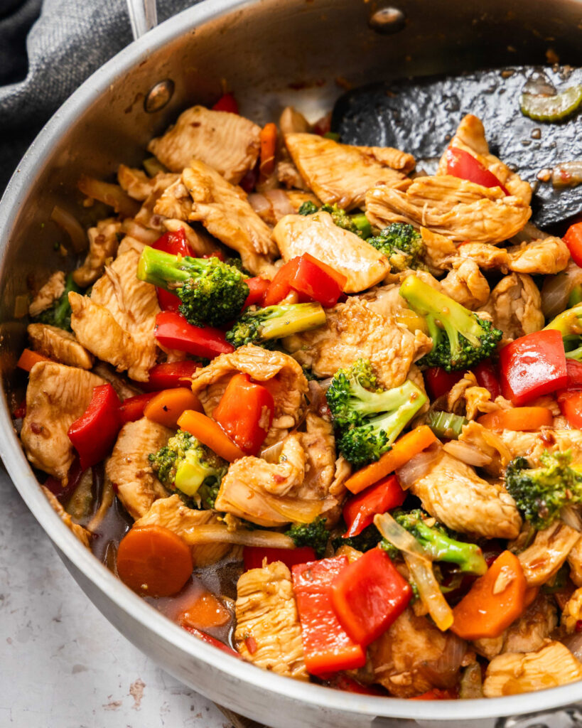 An overhead view of hunan chicken in a large skillet with a wooden spatula.