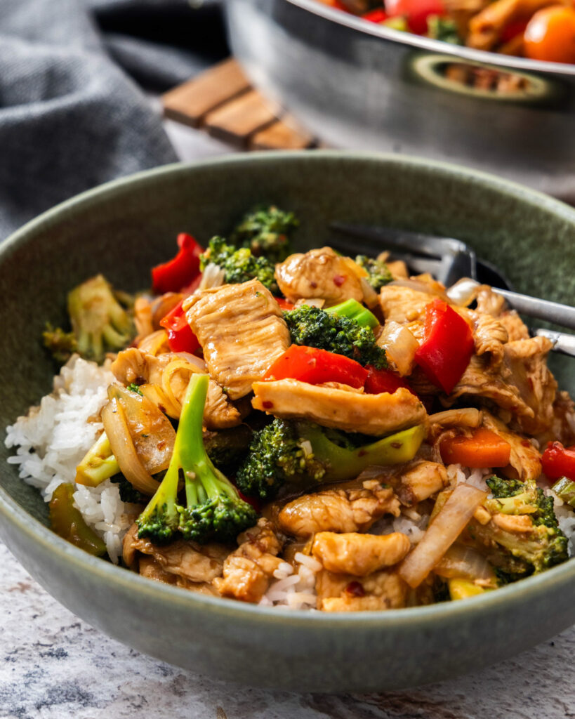 A close up view of huanan chicken in a bowl with rest of the hunan chicken in a skillet in the background.