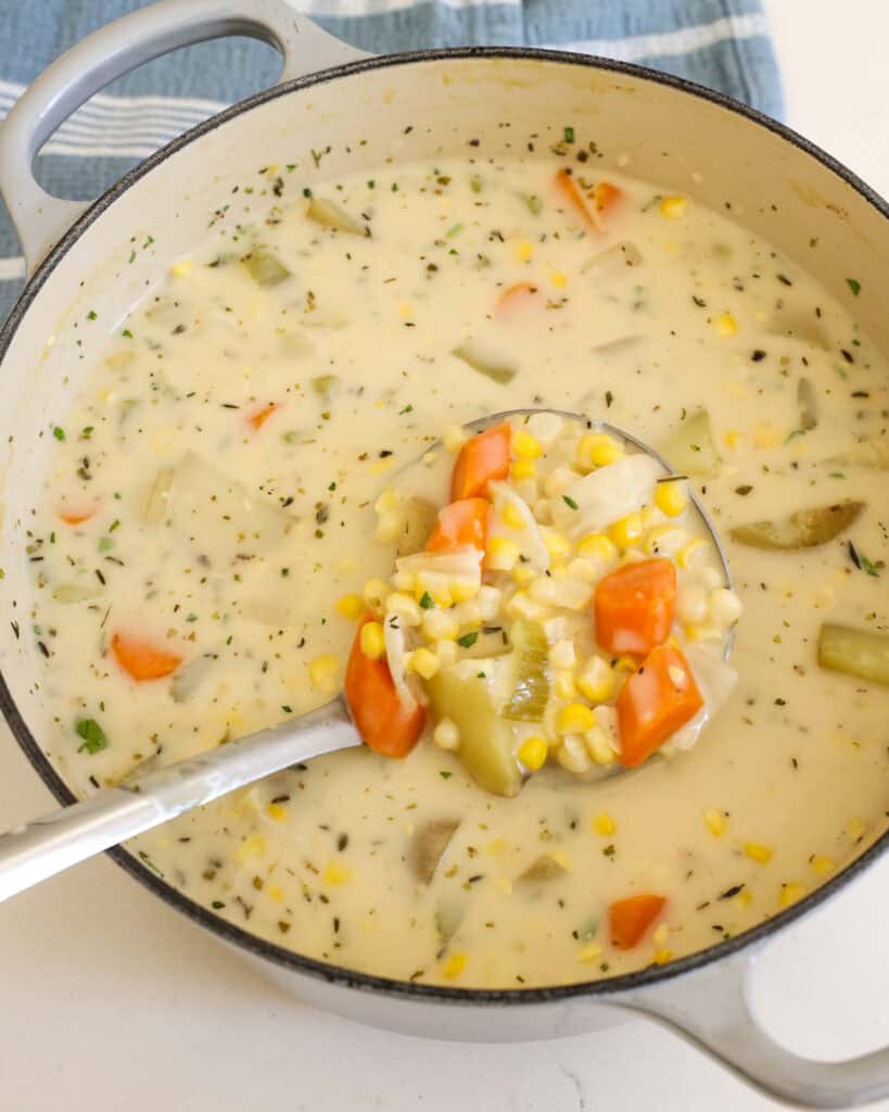 A large Dutch oven and metal ladle full of potato corn chowder.