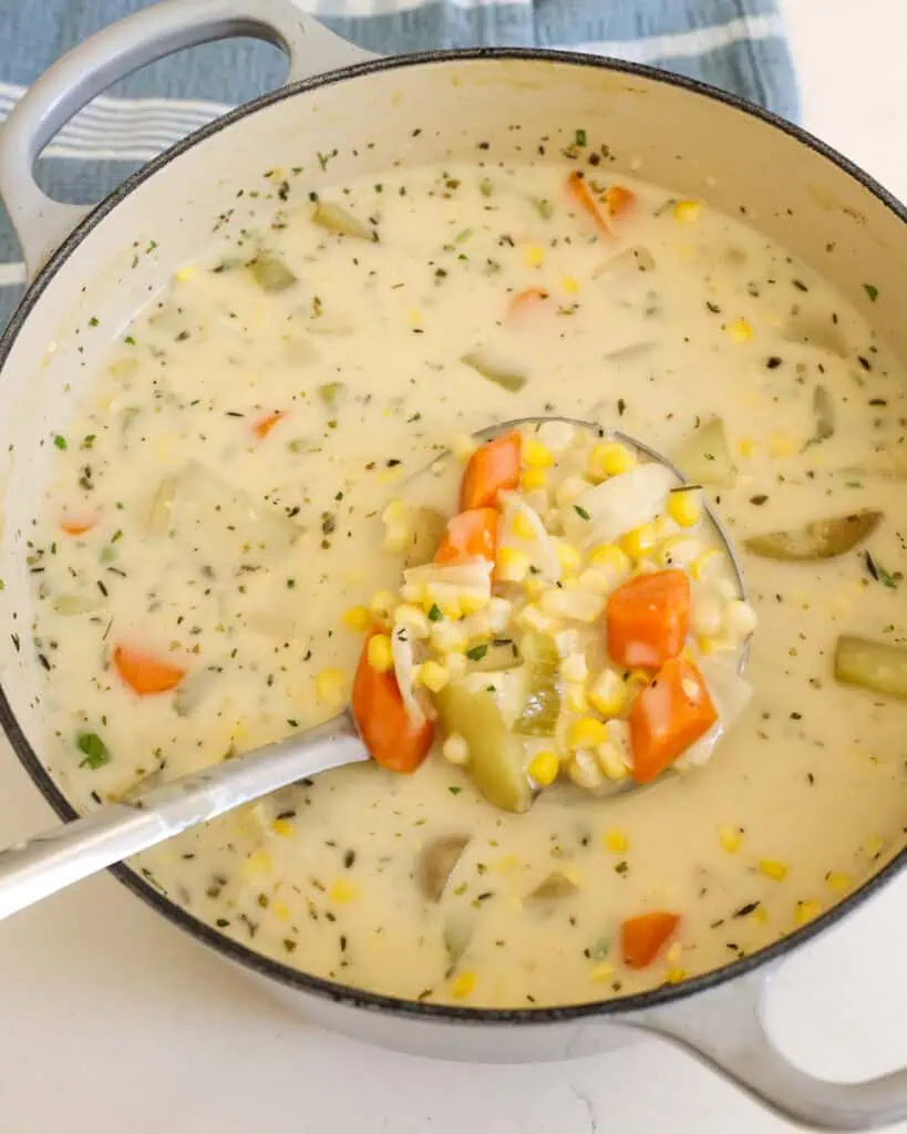 A large Dutch oven and metal ladle full of potato corn chowder. 