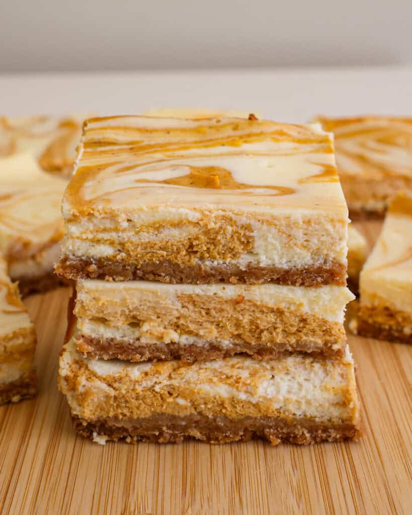 A close up view of three pieces of pumpkin cheesecake bars on a cutting board. 