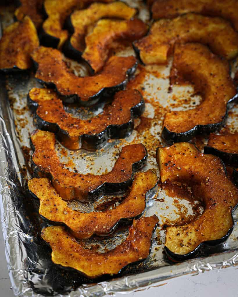 A close up view of roasted acorn squash on a baking sheet covered with lightly oiled aluminum foil. 