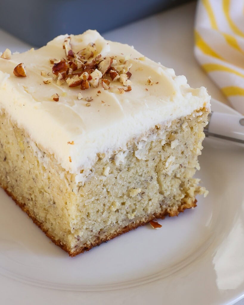 A close up view of a piece of banana cake with cream cheese frosting on a single serving white plate.