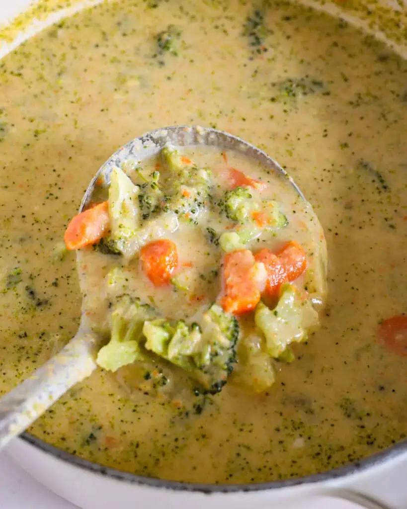 A ladle and Dutch oven full of cheesy broccoli potato soup.