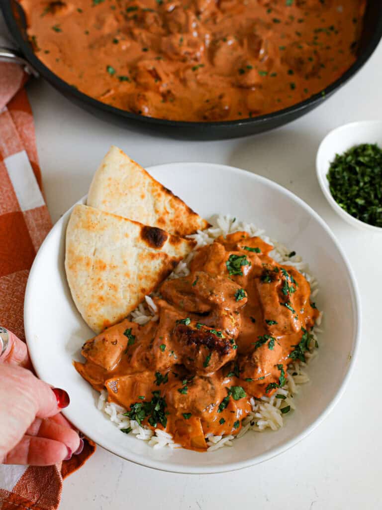 A single serving bowl full of butter chicken over basmati rice, and toasted naan bread. 
