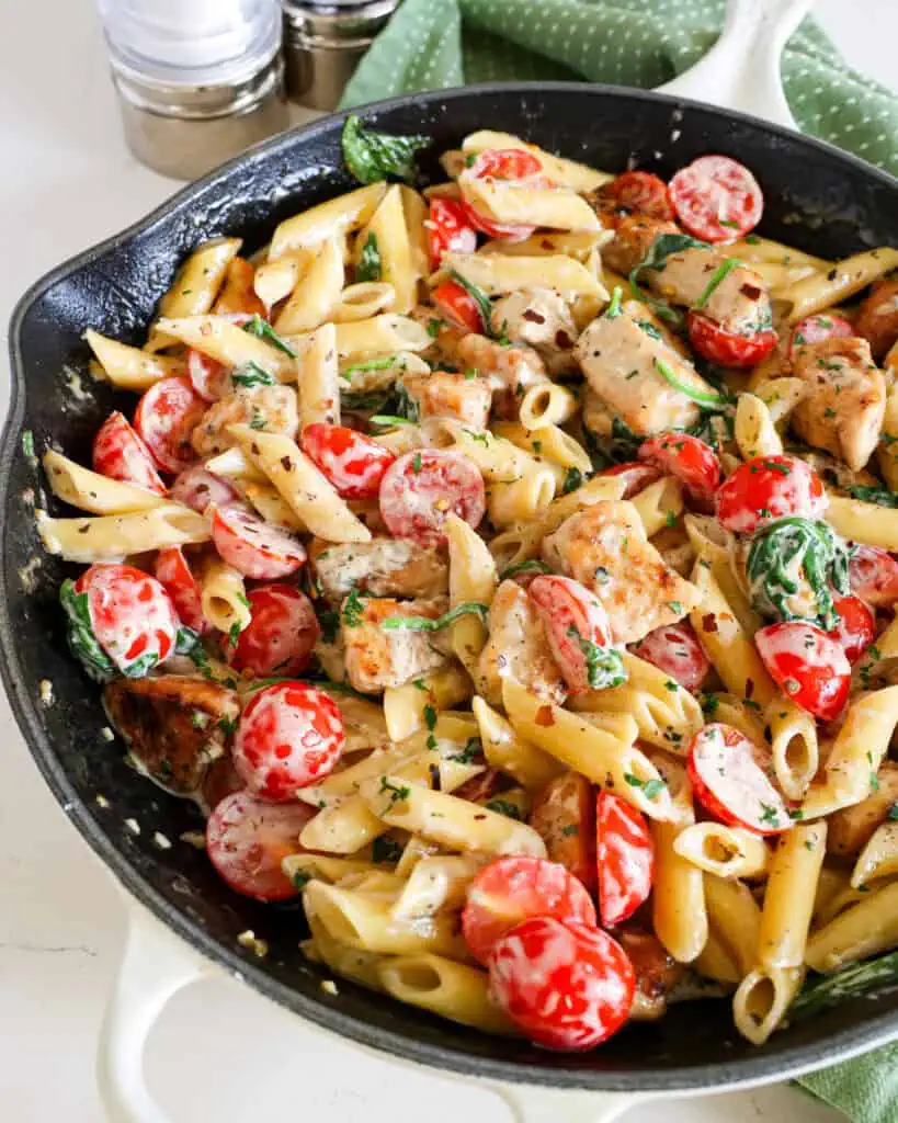 A close up view of chicken penne pasta with tomatoes and spinach in a garlic Parmesan sauce.