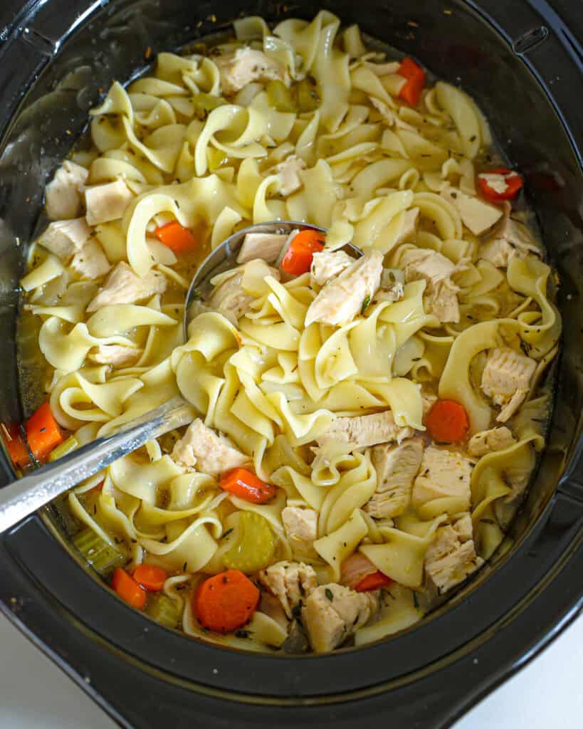 A black crockpot full of chicken noodle soup. 
