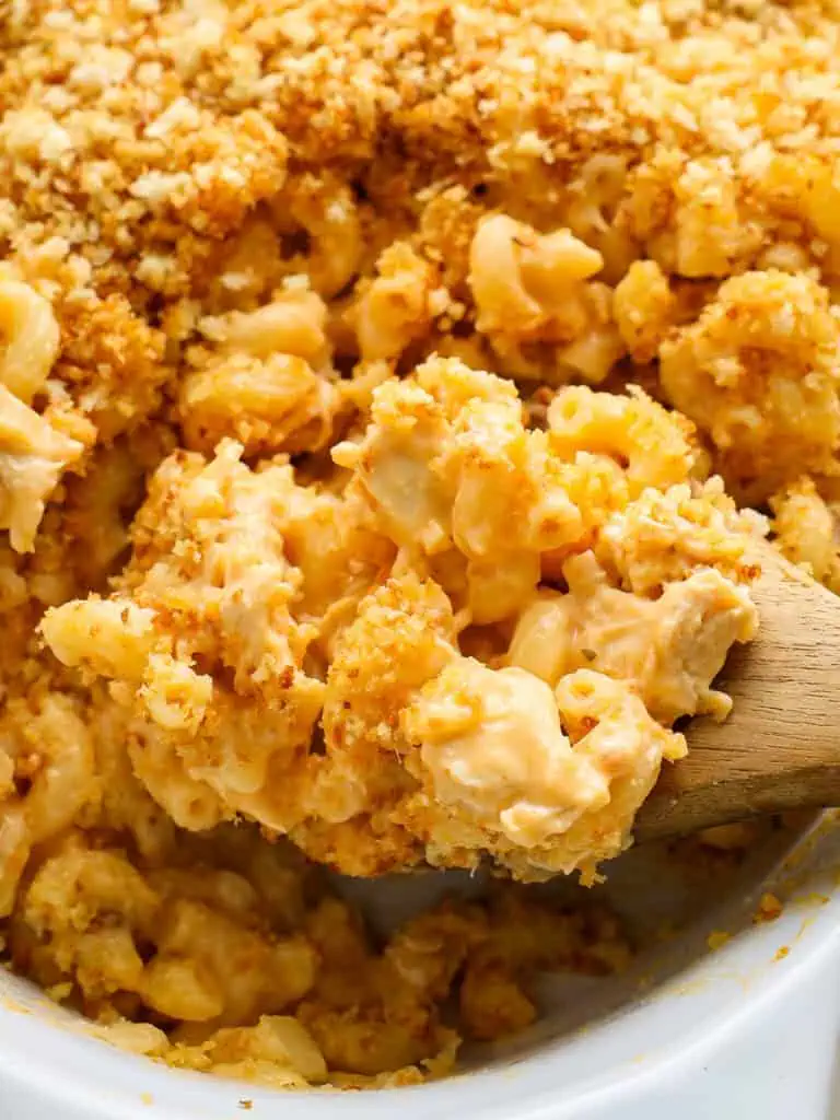 A close up view of a wooden spoon and casserole dish full of Buffalo chicken mac and cheese.