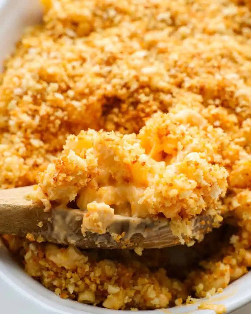 A wooden spoon and a white oval casserole full of Buffalo chicken mac and cheese.