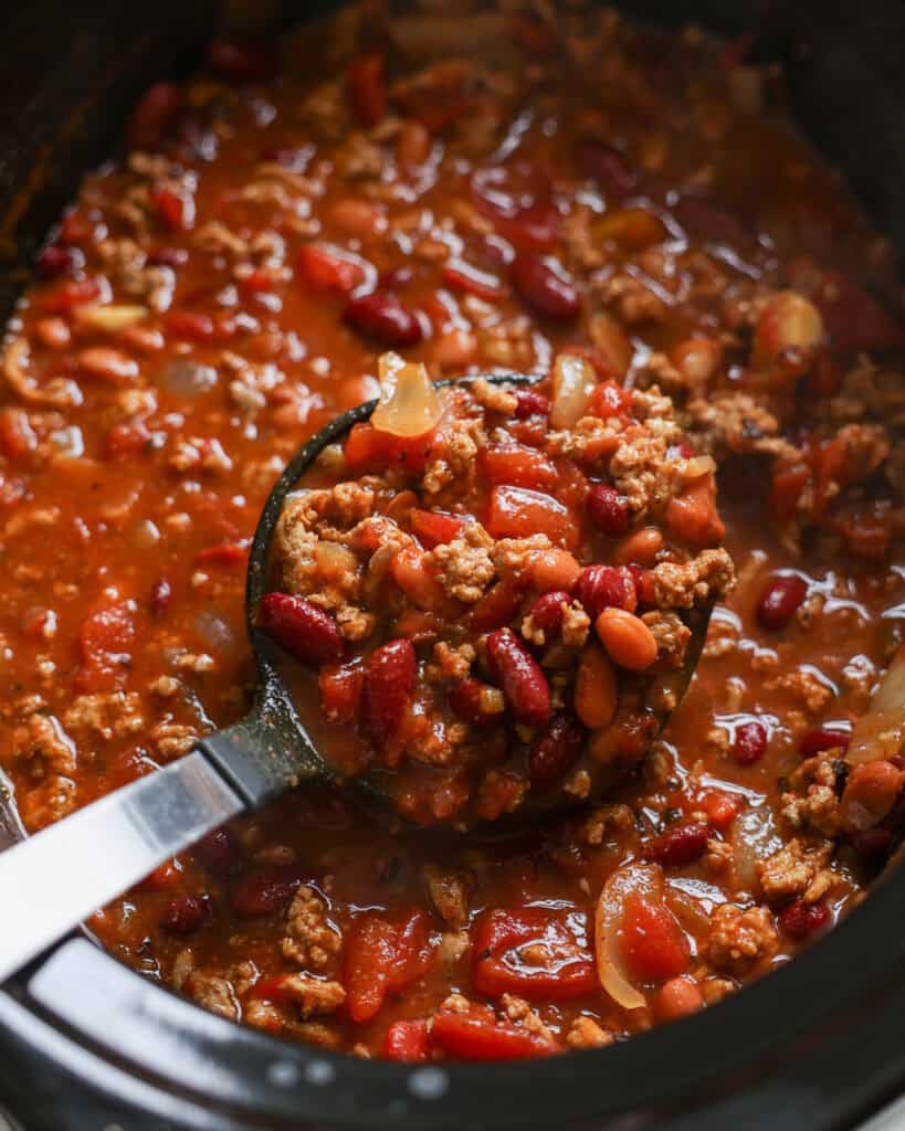 A ladle and a slow cooker full of turkey chili. 
