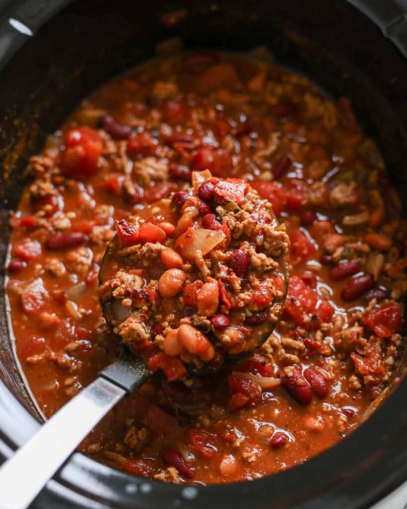 A large black ladle and a crockpot full of ground turkey chili
