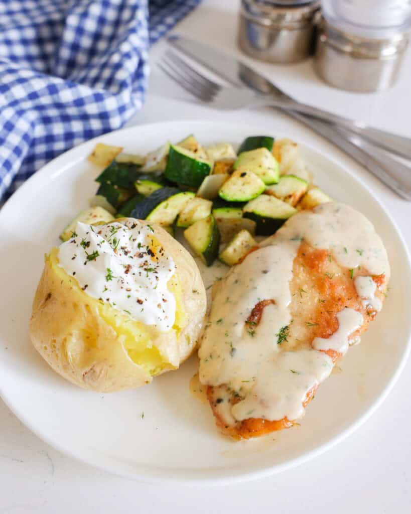 A single serving plate with ranch chicken, a baked potato with sour cream, and sauteed zucchini. 