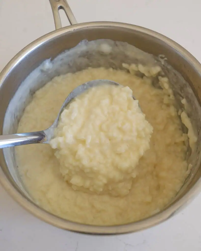 A ladle and a pot full of fresh cooked rice pudding.