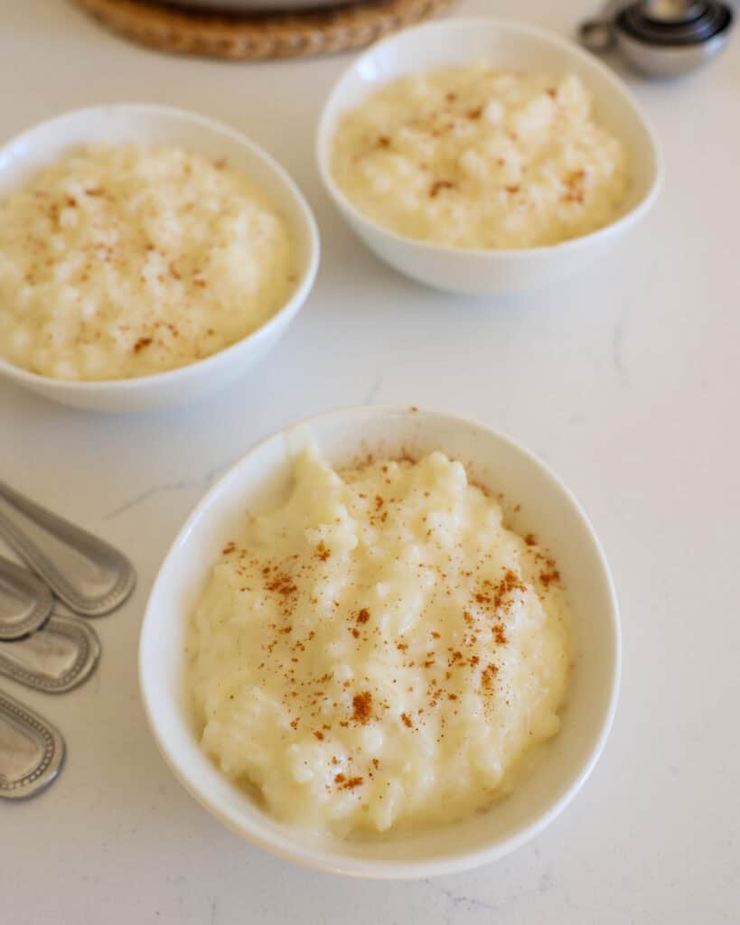 Three small serving bowls full of rice  pudding with spoons off to the side. 