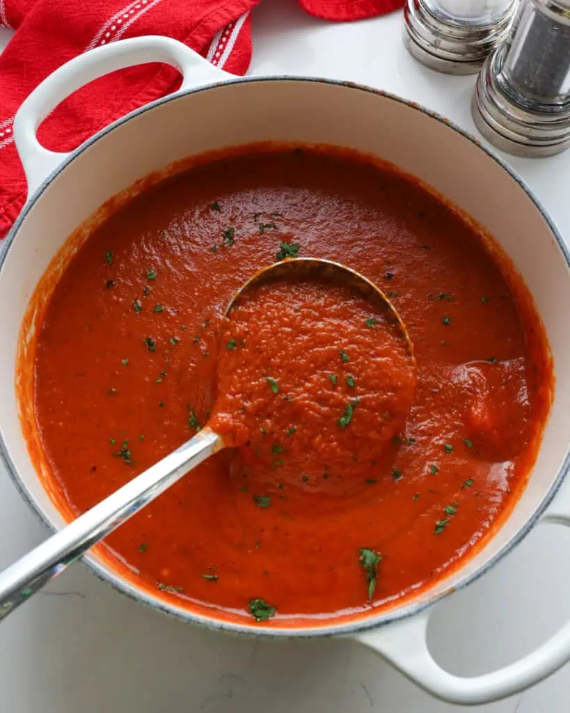 A white Dutch oven and ladle full of roasted red pepper soup.