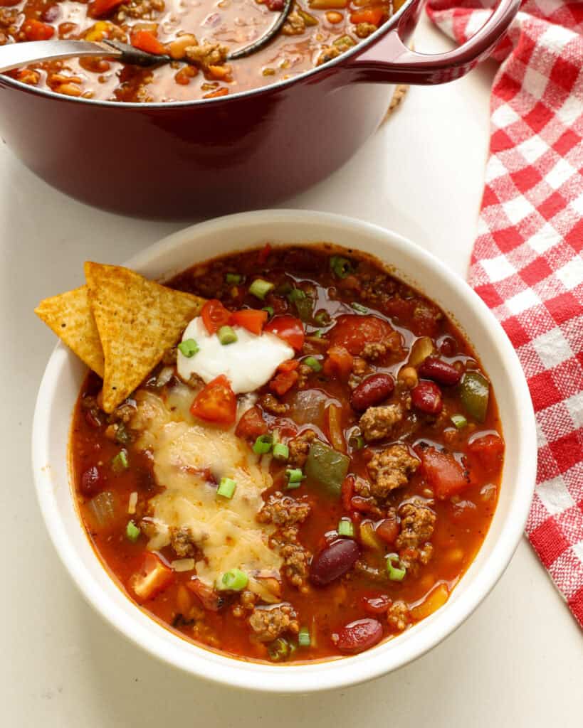 A single serving bowl full of beef chili topped with cheddar, sour cream, and green onions. 